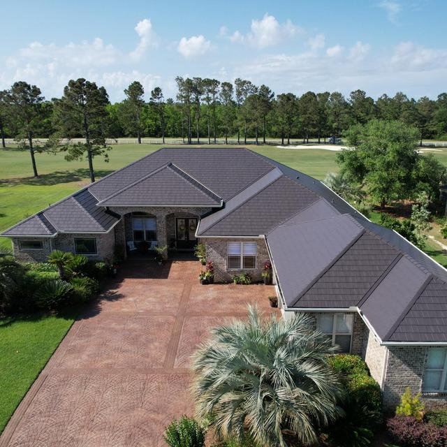 A sprawling home featuring ArrowLine Slate steel roofing in Charcoal Gray, perfectly complementing the stone exterior and lush green landscape.
