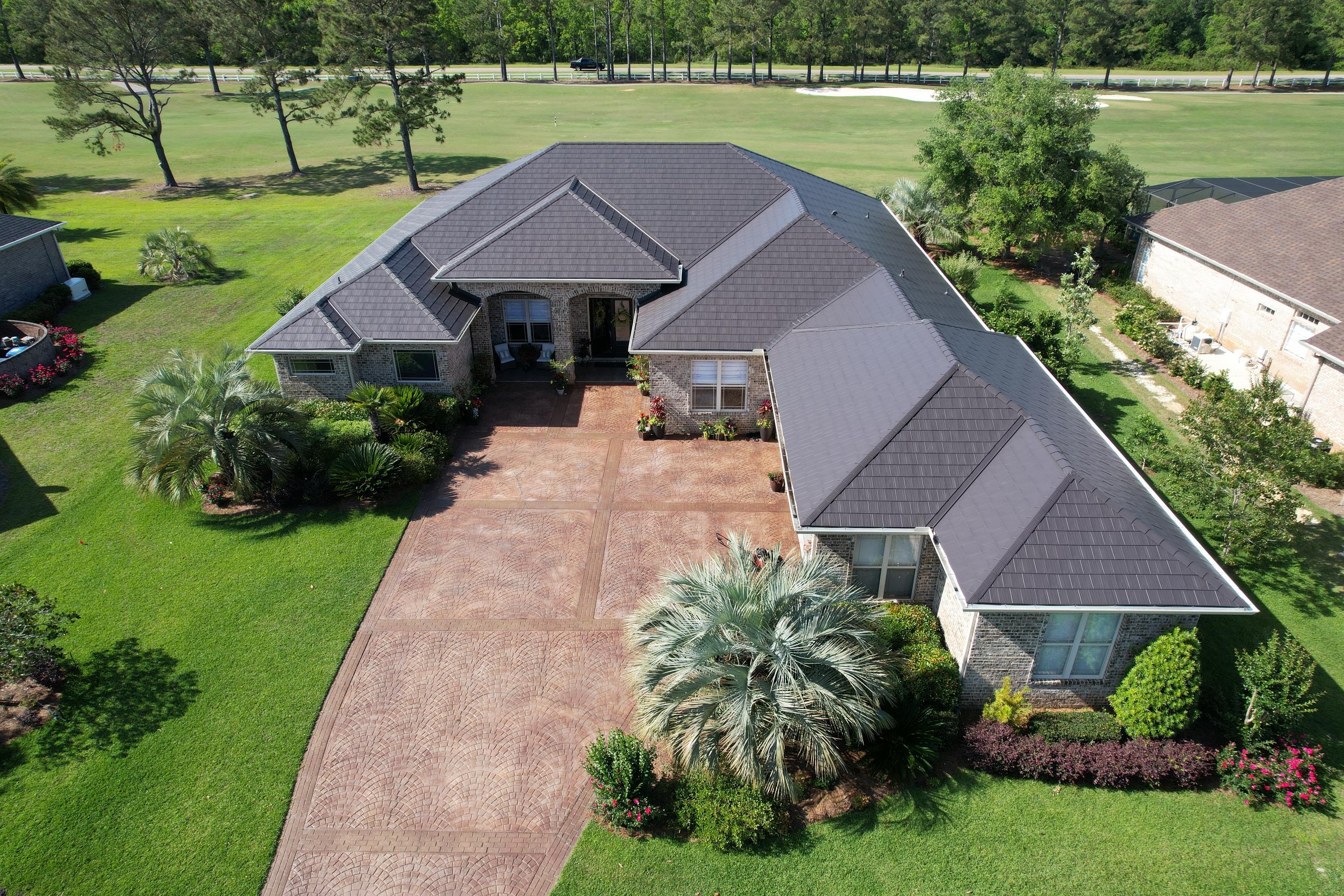 A sprawling home featuring ArrowLine Slate steel roofing in Charcoal Gray, perfectly complementing the stone exterior and lush green landscape.